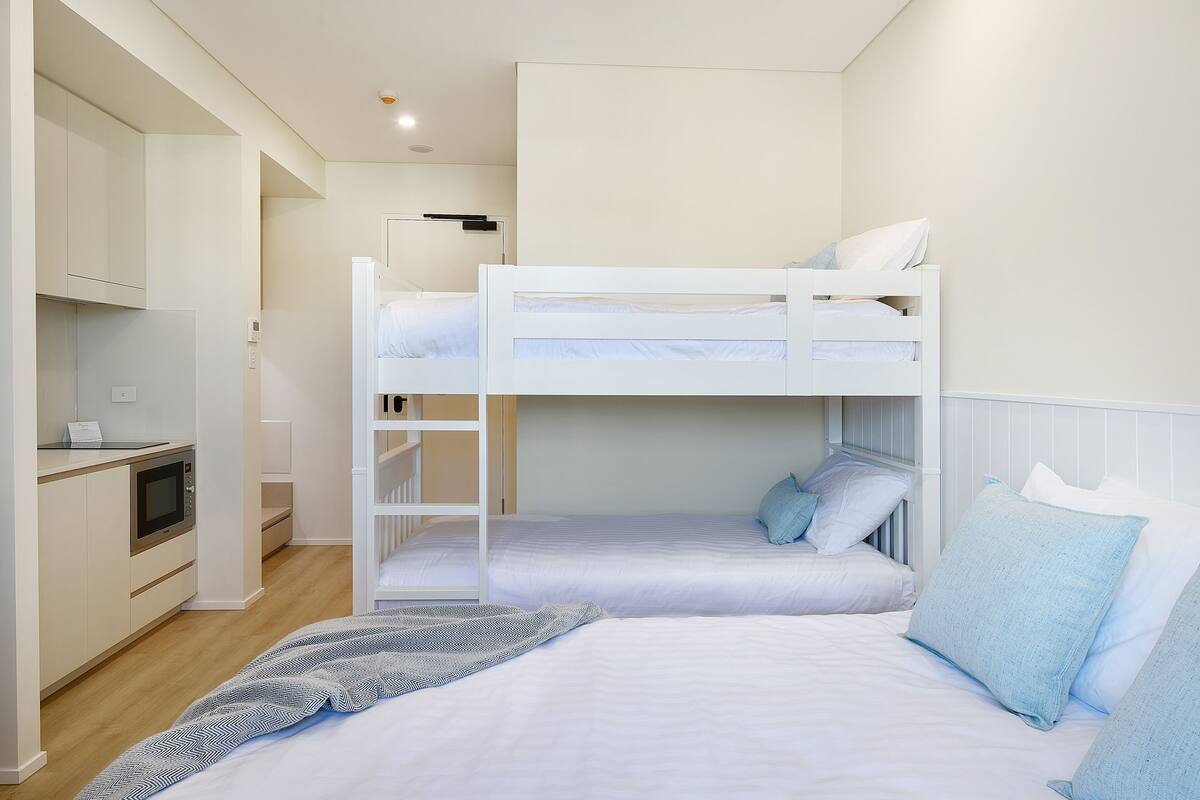 A bunk bed room with a kitchenette, a microwave, and a small desk.