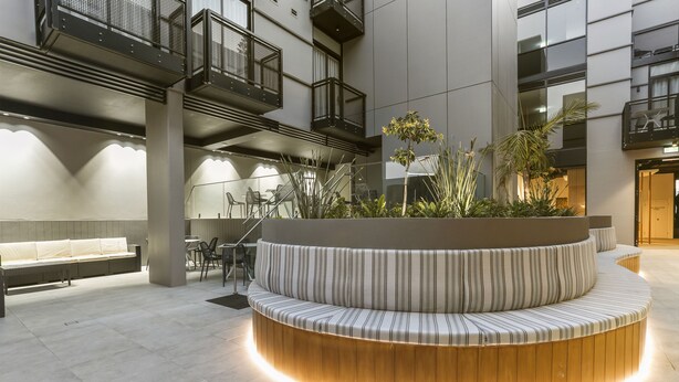 A modern indoor courtyard with a curved seating area, a wooden bench, and a small table with chairs. - Nova Kiama (Kiama)