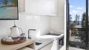 A modern kitchen with a white countertop, a coffee maker, and a view of a tropical beach through the window. - Nova Kiama (Kiama)