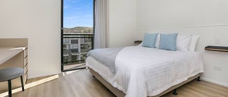 A bedroom with a bed, a desk, and a view of a balcony.
