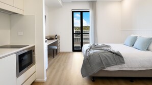 A modern bedroom with a bed, a desk, and a built-in oven. - Nova Kiama (Kiama)