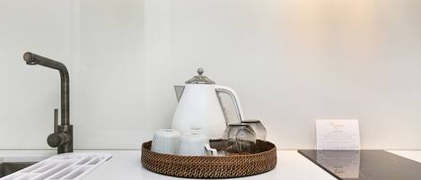 Een aanrecht met een koffiezetapparaat, een waterkoker en een mand met opgerolde handdoeken.