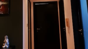Een hal met een houten vloer, een donkere deur aan het einde en een klein beeldje aan de linkerkant.