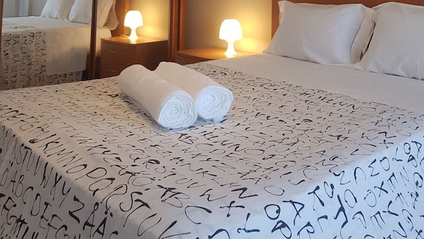Een hotelkamer met een bed, twee bedlampen, een spiegel, en een net opgemaakt bed met opgerolde handdoeken.