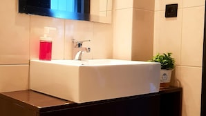 Een moderne badkamer met een wit wastafelmeubel, een spiegel erboven en een kleine plant in een pot op het aanrecht.