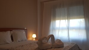 Een hotelkamer met een bed, een nachtkastje met een lamp en een raam met dunne gordijnen.