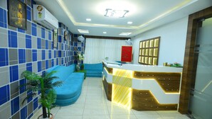 A reception area with a blue and white tiled wall, a reception desk, a blue sofa, and a potted plant. - Hotel Royal Residency (Vadodara)