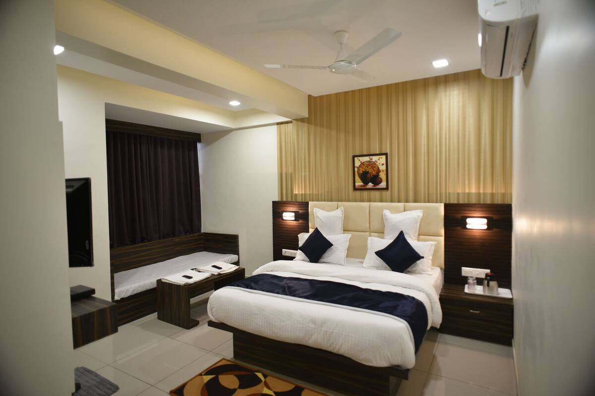 A modern hotel room with a large bed, bedside tables, a ceiling fan, and an air conditioning unit.