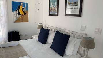 A hotel room with a large bed, two pillows, a nightstand with a lamp, a small table, and a poster on the wall.