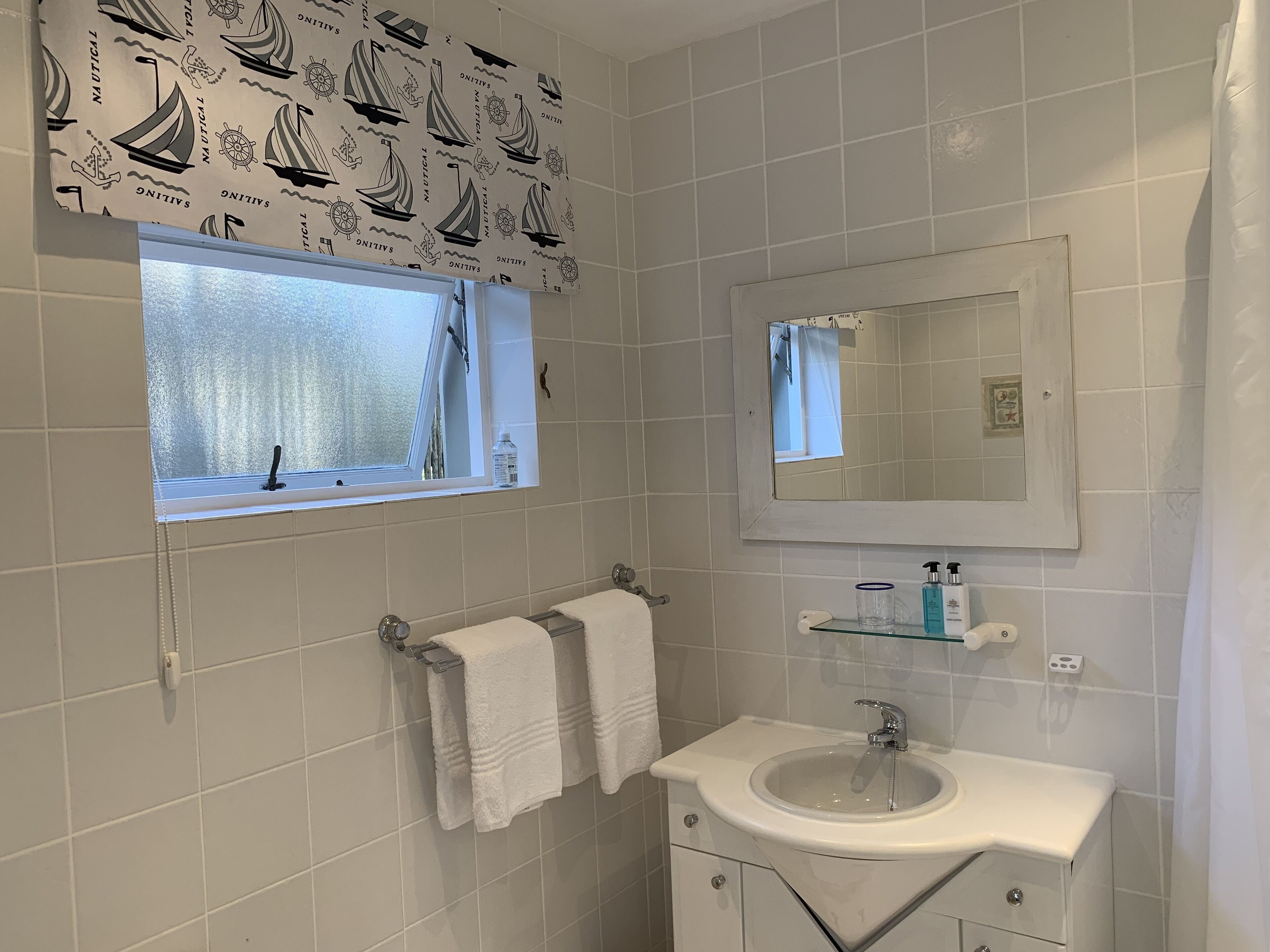 Een badkamer met een raam, een wastafel, een spiegel en een handdoekhouder.