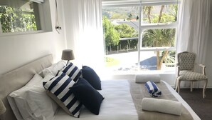Ein ordentlich bezogenes Bett mit gestreiften Kissen, ein Nachttisch mit einer Lampe und ein Sessel mit einem gemusterten Sitzkissen.