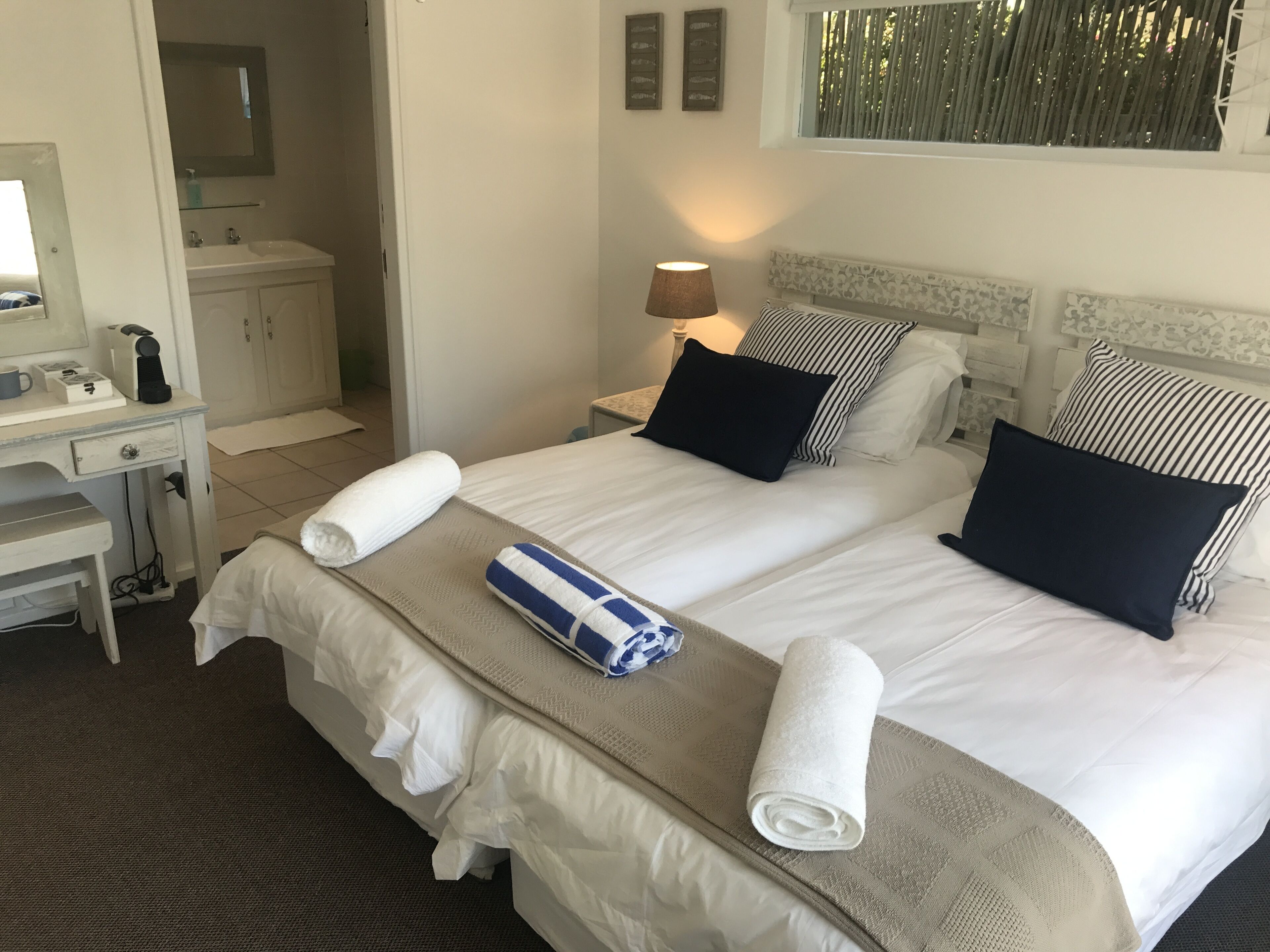 Una habitación de hotel con cama, dos almohadas, una mesita de noche con lámpara, un escritorio con teléfono y un espejo.