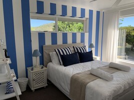 A neatly arranged bedroom with a bed, bedside tables, a lamp, and a view of greenery outside.