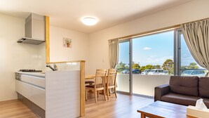 A modern kitchen with a dining area, a sofa, and a view of the parking lot. - The Villas Machidoya (Motobu)