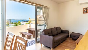A modern living room with a sofa, chairs, a table, and a view of the sea through a sliding glass door. - The Villas Machidoya (Motobu)