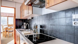A modern kitchen with wooden cabinets, a black tiled backsplash, a built-in stove, and a window overlooking a snowy landscape.