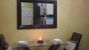 Un coin repas avec une table en verre, deux chaises, une bougie et un lustre.