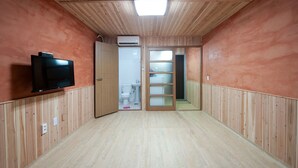 Une pièce aux murs recouverts de lambris en bois, dotée d’un téléviseur à écran plat fixé au mur et d’une porte donnant accès à une salle de bain.