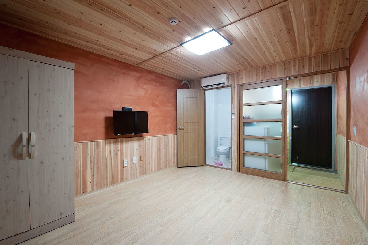 Une pièce aux murs recouverts de lambris en bois, avec un téléviseur à écran plat fixé au mur, une armoire en bois et une porte coulissante en verre donnant sur une salle de bain.