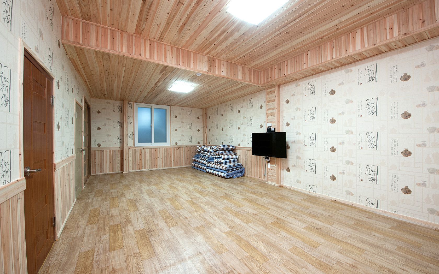 Een ruime kamer met houten vloeren, een aan de muur bevestigde televisie en een raam met gezandstraald glas.