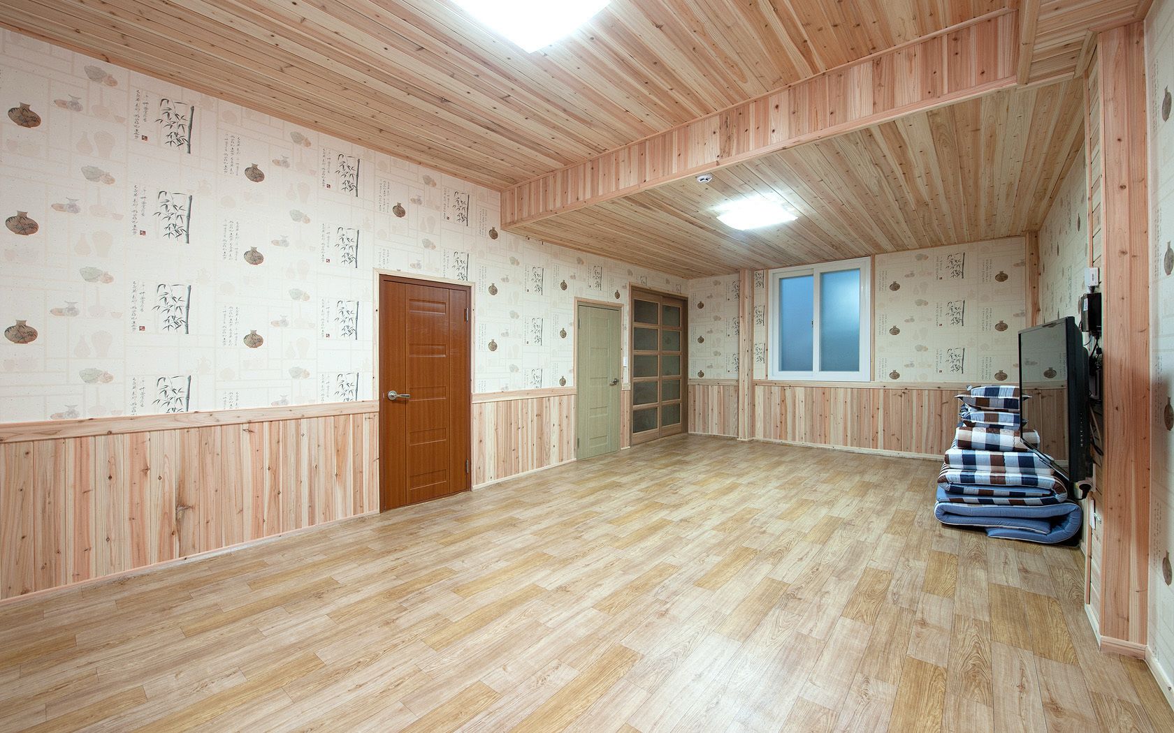 Un'ampia stanza con pavimento in legno, una porta in legno, una finestra e un televisore montato a parete.