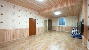 Un'ampia stanza con pavimento in legno, una porta in legno, una finestra e un televisore montato a parete.