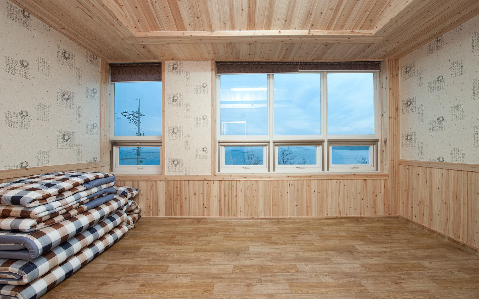 A room with wooden walls and floors, large windows, and a view of the sky.