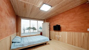 Une chambre avec un lit, un téléviseur fixé au mur et une fenêtre donnant sur des arbres.