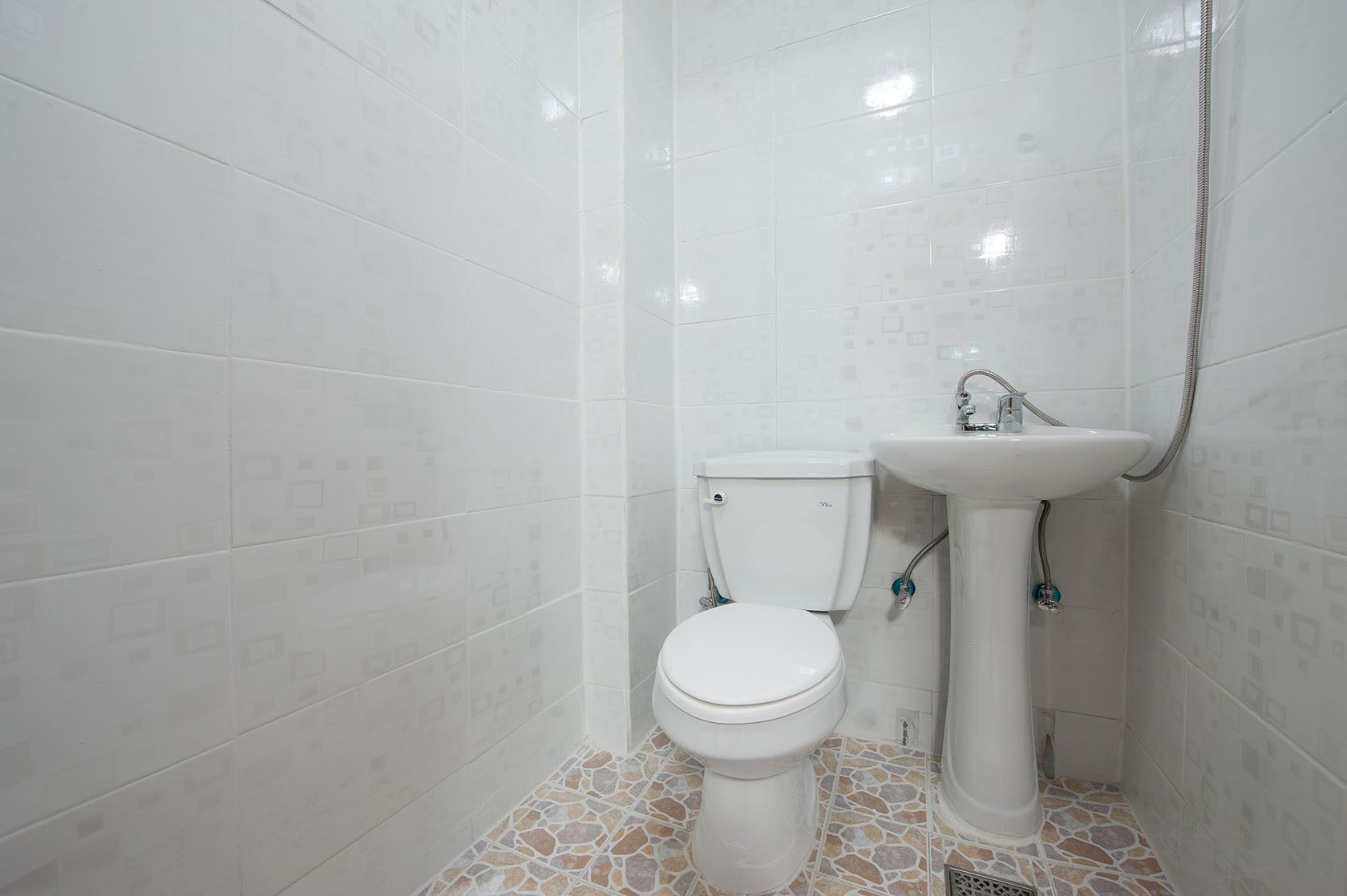 Une salle de bain avec des murs carrelés de carreaux blancs, des toilettes et un lavabo sur colonne avec un robinet.