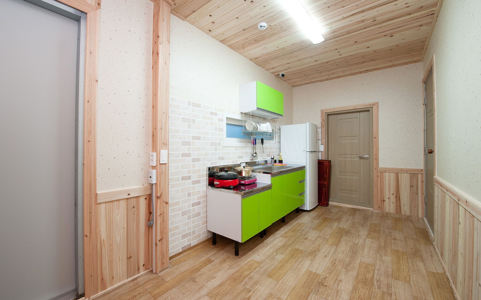 A narrow hallway with a kitchen area featuring a green countertop, a white refrigerator, and a red appliance.