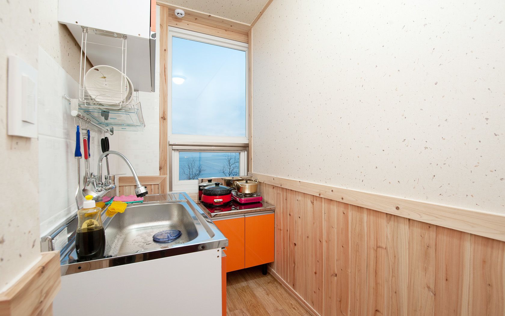 Een kleine keuken met een spoelbak, houten kastjes en een raam.