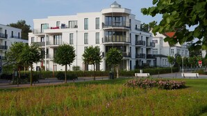 A modern multi-story building with balconies and large windows, surrounded by greenery and a well-maintained lawn.