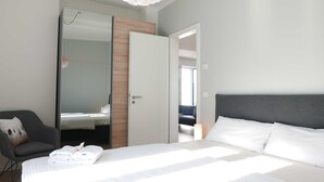 A modern hotel room with a large bed, a chair, a wardrobe, and a mirror.