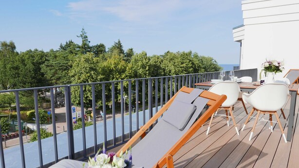 A balcony with a wooden deck, white lounge chairs, and a table set for dining.