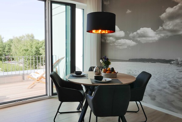 A dining area with a round table, black chairs, a black pendant light, a bowl of fruit, and a vase with flowers.