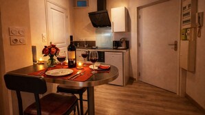 A compact kitchen with a dining area, featuring a table set for two with wine glasses, a candle, and a bottle of wine. - Belterre Studio – Between Sky & Sea (Boulogne-sur-Mer)