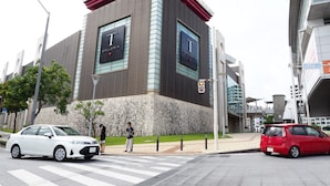 A modern building with a prominent 'I GALLERIA' sign, a crosswalk, and cars on the street. - Holiday Homes TSUBOYA 2nd (Naha)