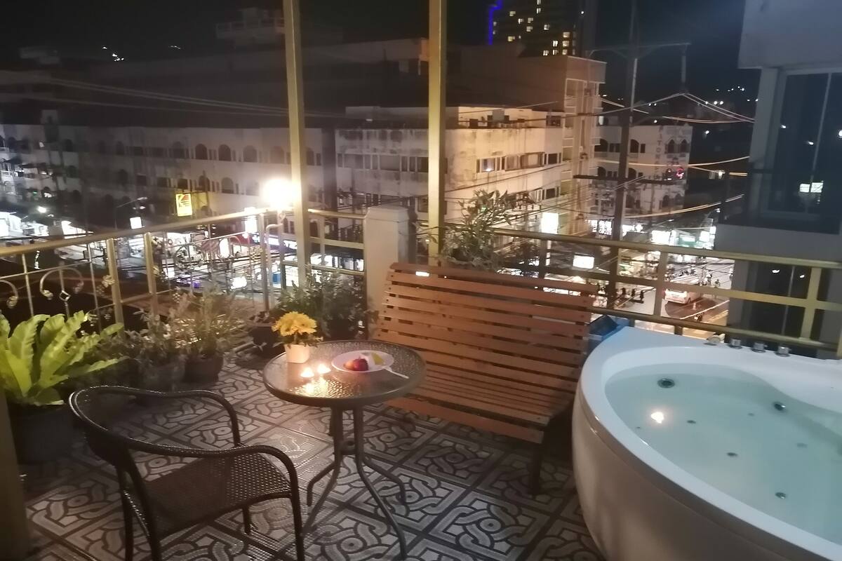 A balcony with a hot tub, a table with a flower vase, and potted plants.
