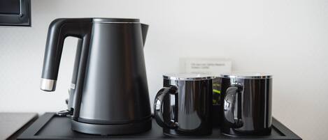 A black electric kettle and two black mugs on a black tray.