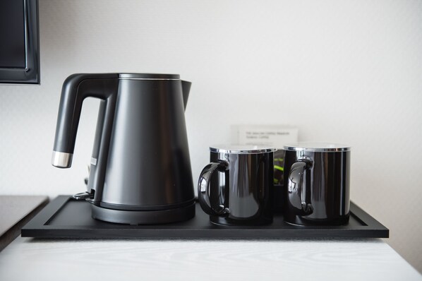 Una tetera eléctrica negra y dos tazas negras sobre una bandeja negra.