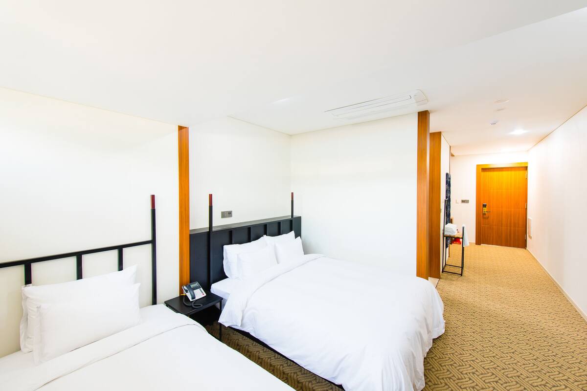 A hotel room with two beds, a nightstand, a wooden door, and a carpeted floor.