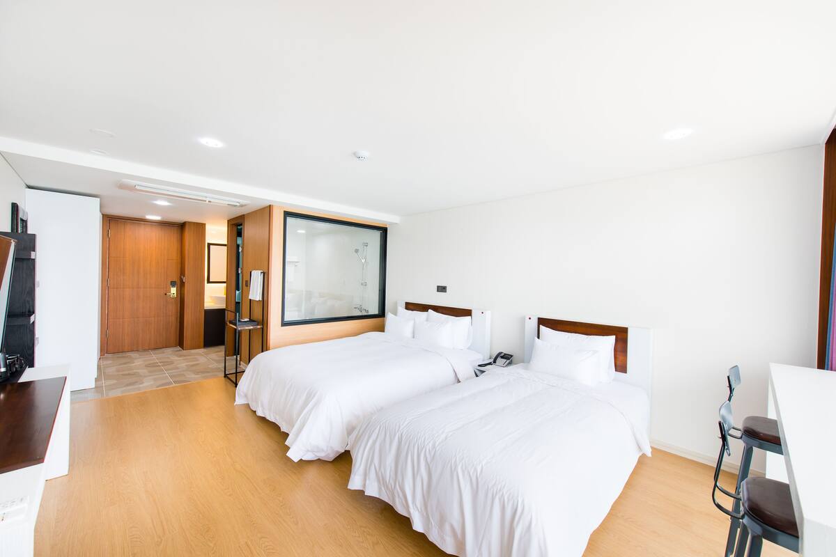 A hotel room with two beds, a desk, a chair, and a large window.