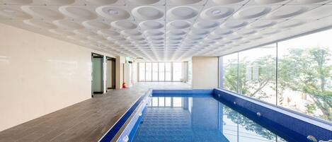 A modern indoor swimming pool with a blue tiled floor and a ceiling with circular patterns.