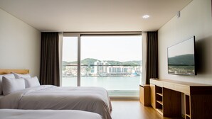 Habitación de hotel con una cama grande, un televisor montado en la pared y vistas a un paisaje urbano por la ventana.