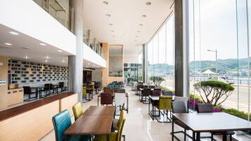 Een modern restaurant met een lange toonbank, meerdere eettafels en stoelen. Grote ramen bieden uitzicht op de skyline.