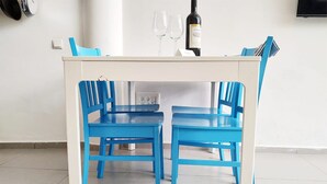 A white table with two blue chairs, a bottle of wine, and two wine glasses on top. - AirTLV Centrally Located Studio With Gallery (Tel Aviv)