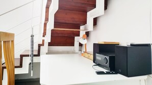 A modern interior with a white staircase, wooden panel walls, and a flat-screen TV on a white table. - AirTLV Centrally Located Studio With Gallery (Tel Aviv)