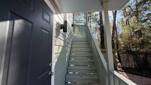 A staircase leading to a dark door, surrounded by a wooden fence and trees. - Spacious 1BR Apt Retreat in The Woodlands: Private, Peaceful, Great Location (Spring)