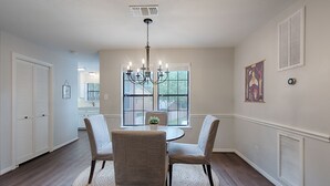 A dining area with a round table, four chairs, a chandelier, and a view through large windows. - Spacious 1BR Apt Retreat in The Woodlands: Private, Peaceful, Great Location (Spring)