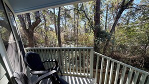 A covered porch with a black chair and a wooden railing overlooking a forested area. - Spacious 1BR Apt Retreat in The Woodlands: Private, Peaceful, Great Location (Spring)